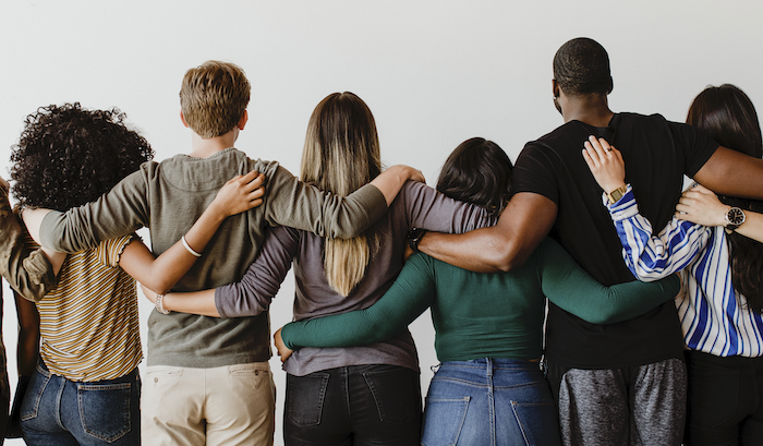 Imagem em meio-corpo de pessoas de costas se abraçando, várias etnias, fundo branco