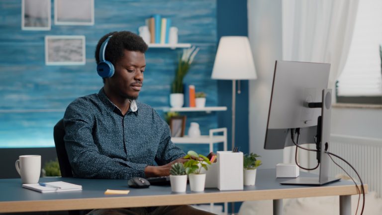Rapaz negro, com fones de ouvido, em fundo azul, desfrutando novas regras do teletrabalho, em home office